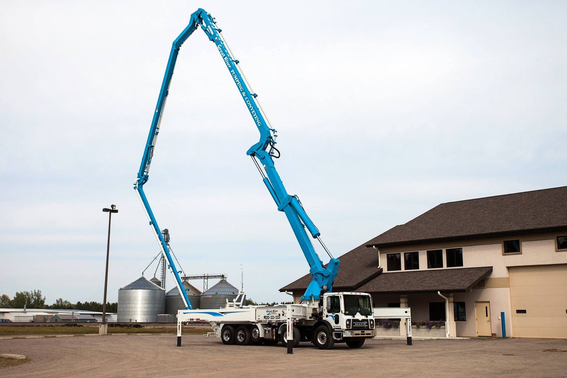 Concrete pump truck with long blue boom extended beside a building on a construction site