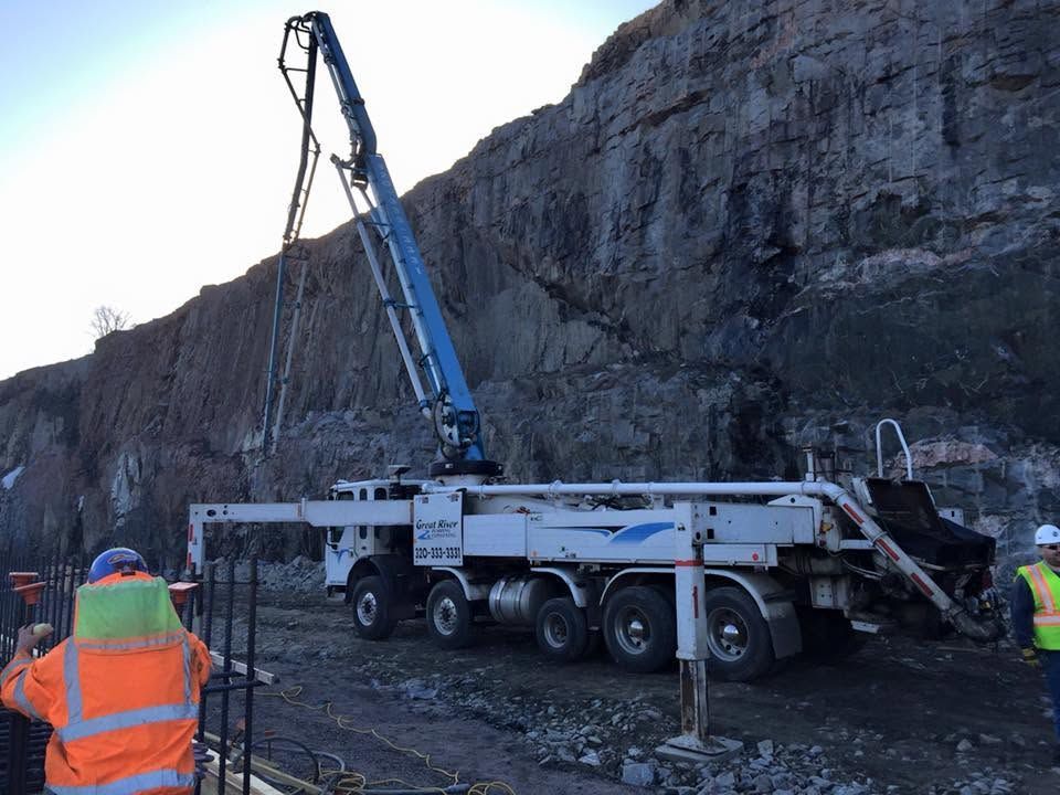 Utility truck with raised boom beside a rocky cliff, with workers in orange safety vests.