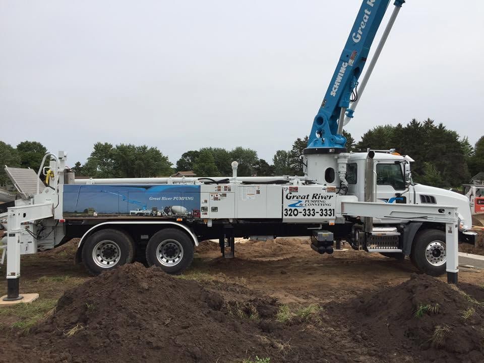 Blue utility truck with boom arm parked on muddy ground near a dirt pile outdoors
