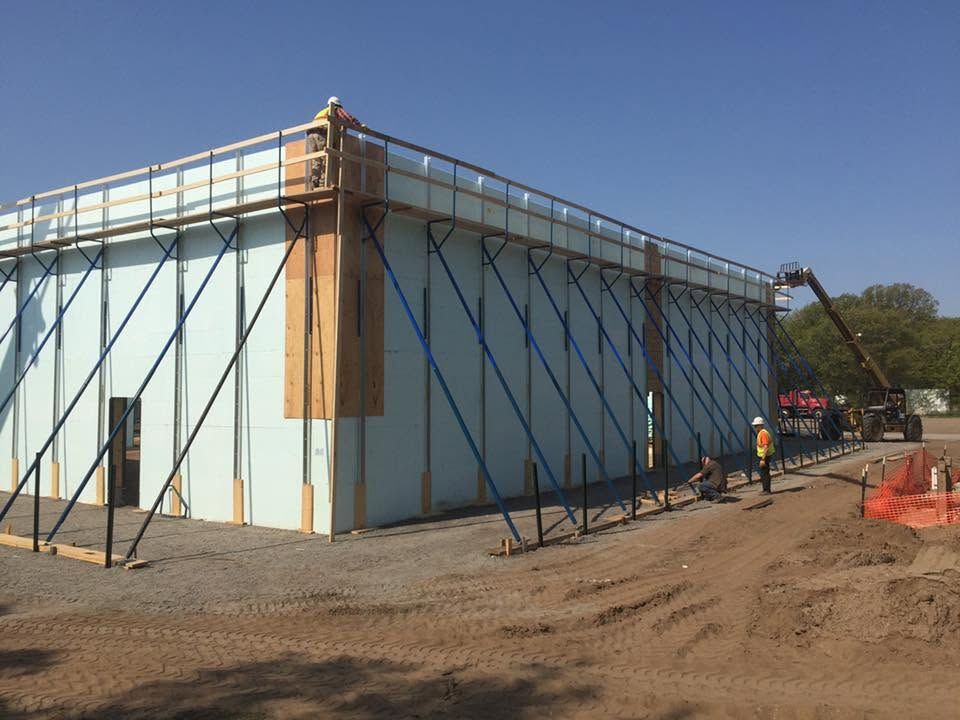 Large white construction enclosure with black support poles on a dirt lot under a clear blue sky.