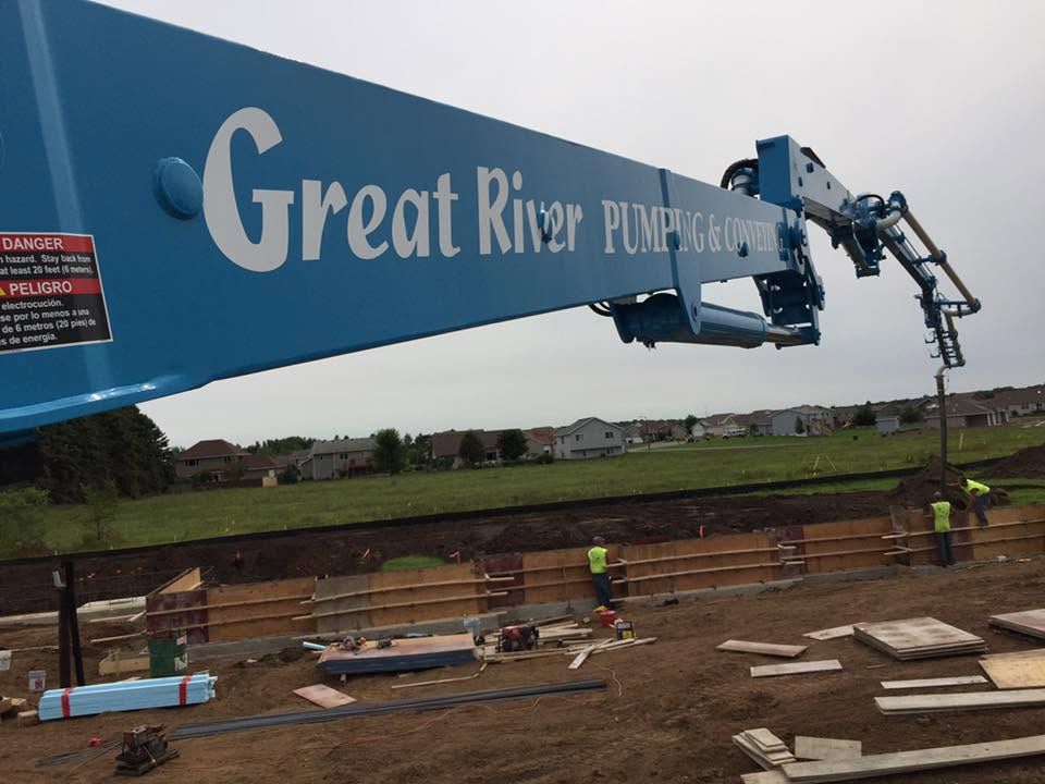 Crane lifting a large blue Great River Pumping sign over a construction site with workers below