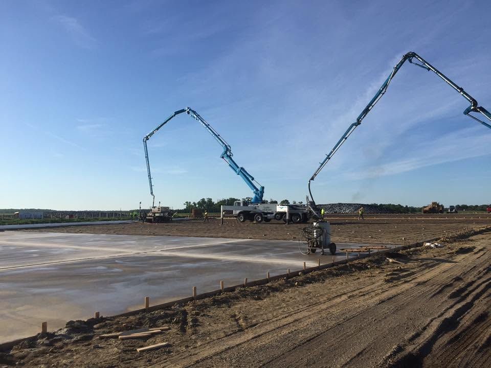 Two concrete pump trucks pouring concrete across a large construction site under a blue sky