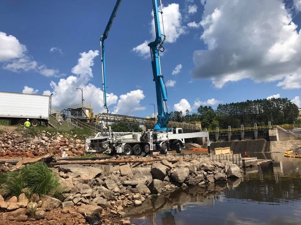Blue crane working beside rocky shoreline and water under a partly cloudy sky