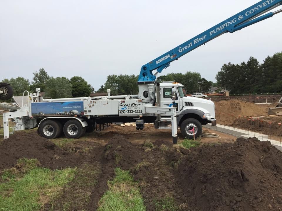 White dump truck with blue crane arm on a muddy construction site carrying dirt under overcast skies
