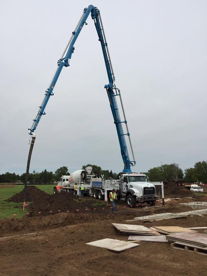 Concrete pump truck pouring at a construction site, with a long blue boom over a dirt mound.