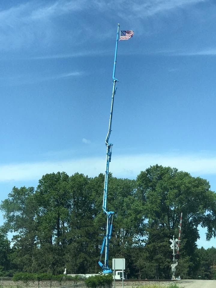 Tall blue cherry picker extended high with a small U.S. flag against a blue sky near trees and a basketball hoop