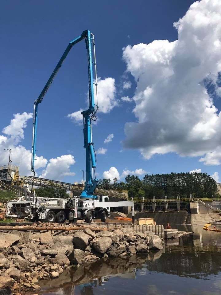Concrete pump truck pouring concrete at a rocky waterfront construction site under a blue sky