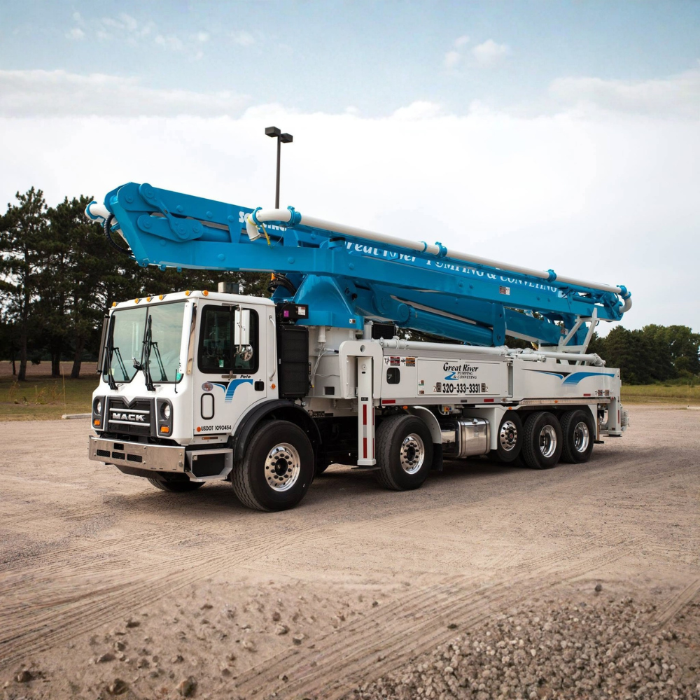 Blue concrete pump truck parked on a gravel lot under a cloudy sky