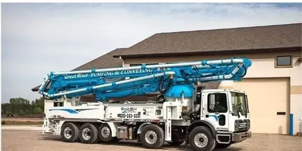 Blue concrete pump truck parked outside a warehouse