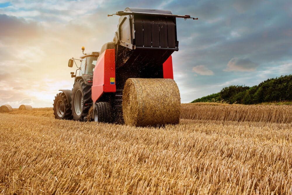 A Tractor Is Baling Hay in A Field — Parkes Machinery Services PTY LTD in Parkes, NSW