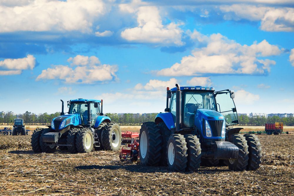 Two Blue Tractors Are Plowing a Field on A Sunny Day — Parkes Machinery Services PTY LTD in Orange, NSW