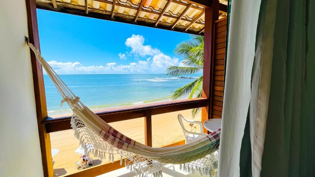 Rede junto à janela com vista para a água turquesa e o céu azul, à beira-mar.
