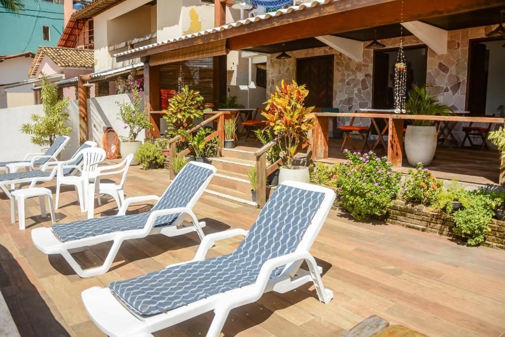Deck de madeira ao ar livre com espreguiçadeiras brancas, mesas e um pátio sombreado à beira-mar.