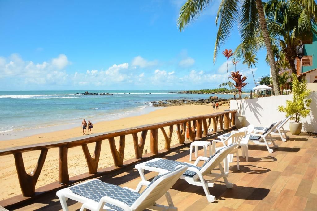 Espreguiçadeiras à beira-mar em um deck tropical ensolarado, ao lado de águas turquesas e palmeiras.