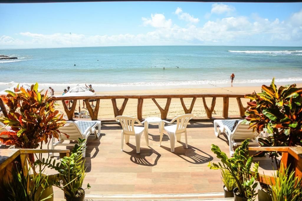 Pátio à beira-mar com cadeiras e mesas brancas com vista para um oceano azul calmo sob um céu ensolarado.