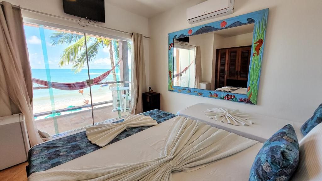 Quarto com vista para a praia, duas camas de solteiro, decoração em tons turquesa e um espelho de parede junto à janela.