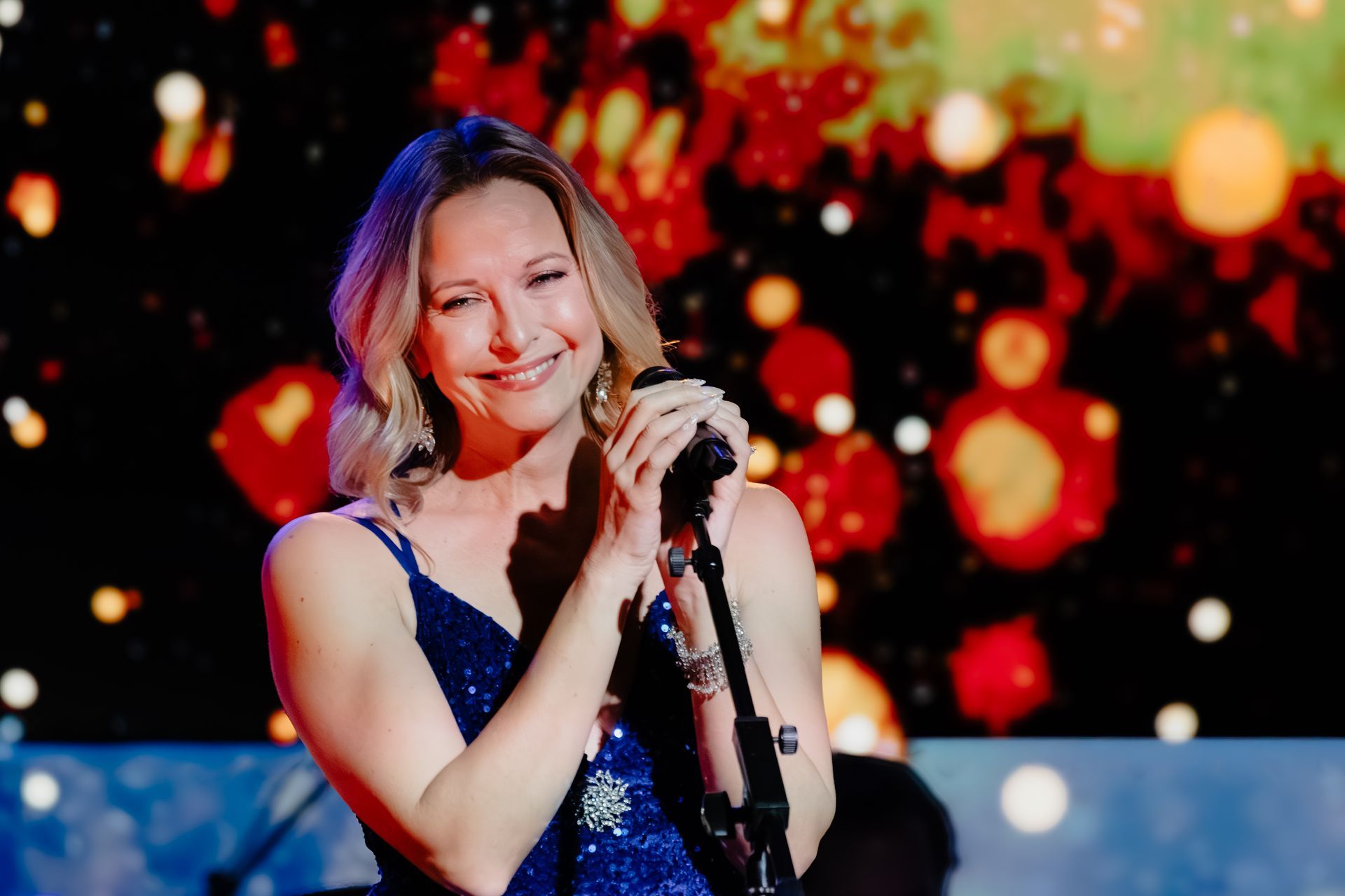 Singer in a blue dress performing into a microphone with warm stage lights behind her