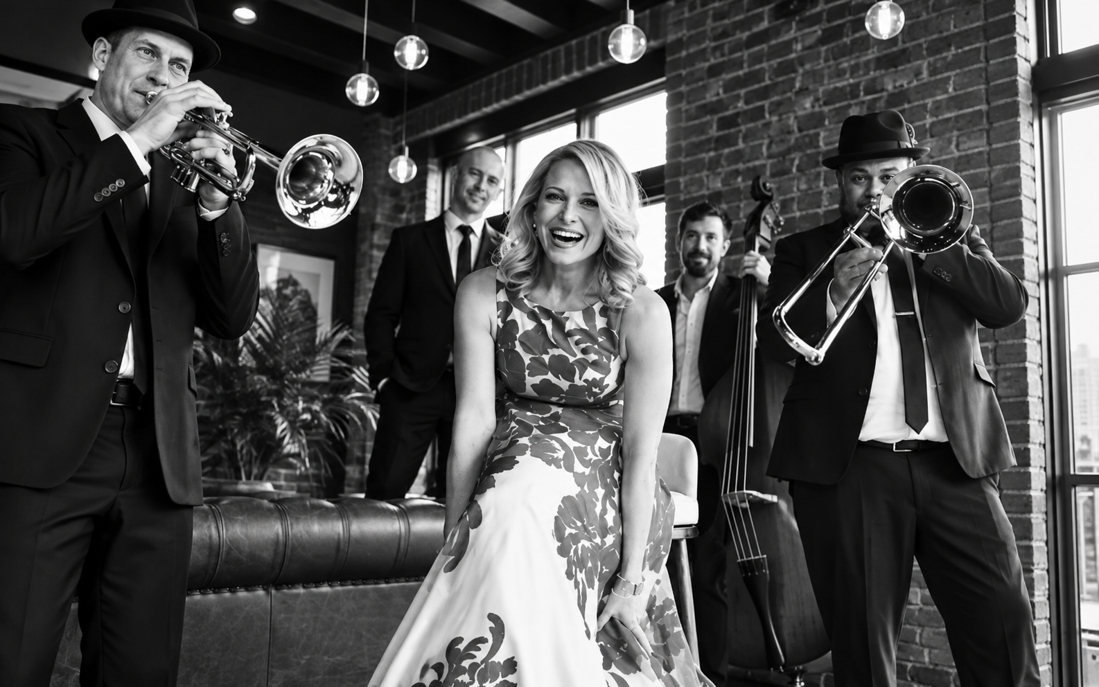Band playing in a lounge with a smiling woman in a floral dress at center stage