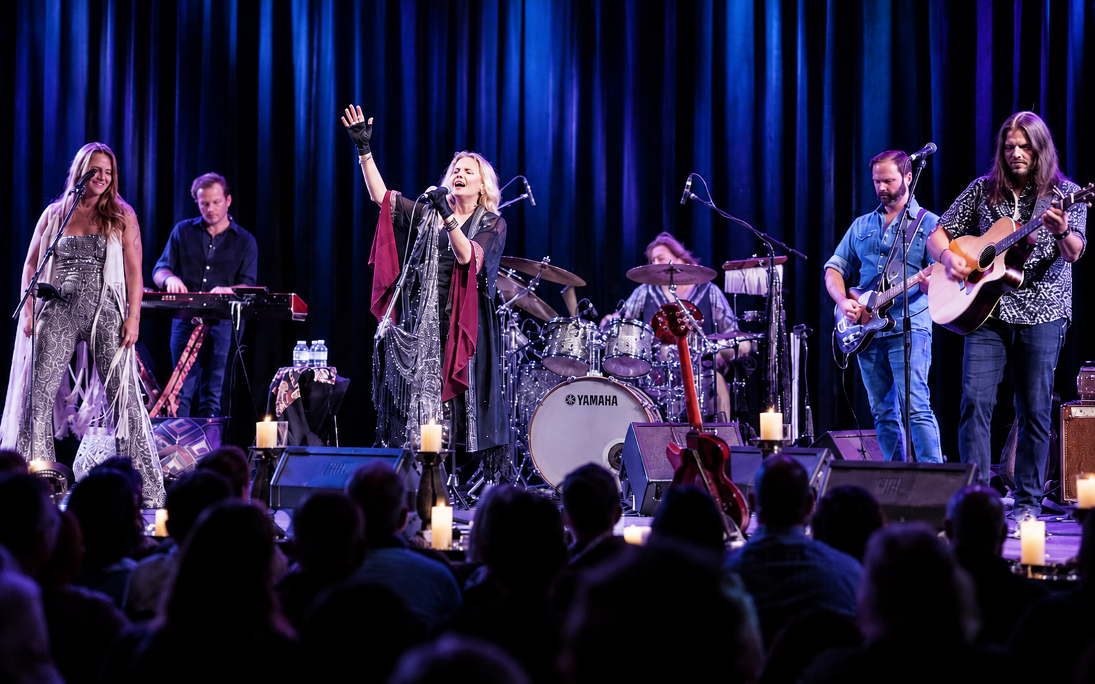 Live band performing on stage under purple lights, with singer center and audience silhouettes in front