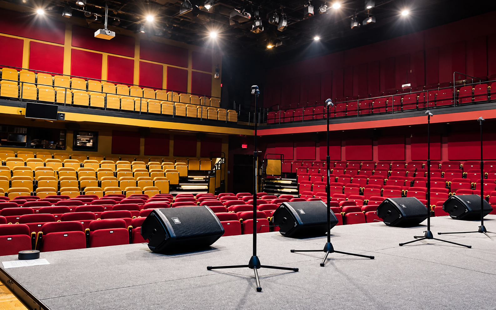 Empty theater stage with microphones and red seats under warm stage lights