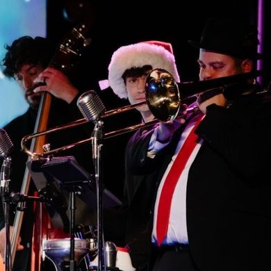 Musicians in hats playing brass and string instruments on a dimly lit stage