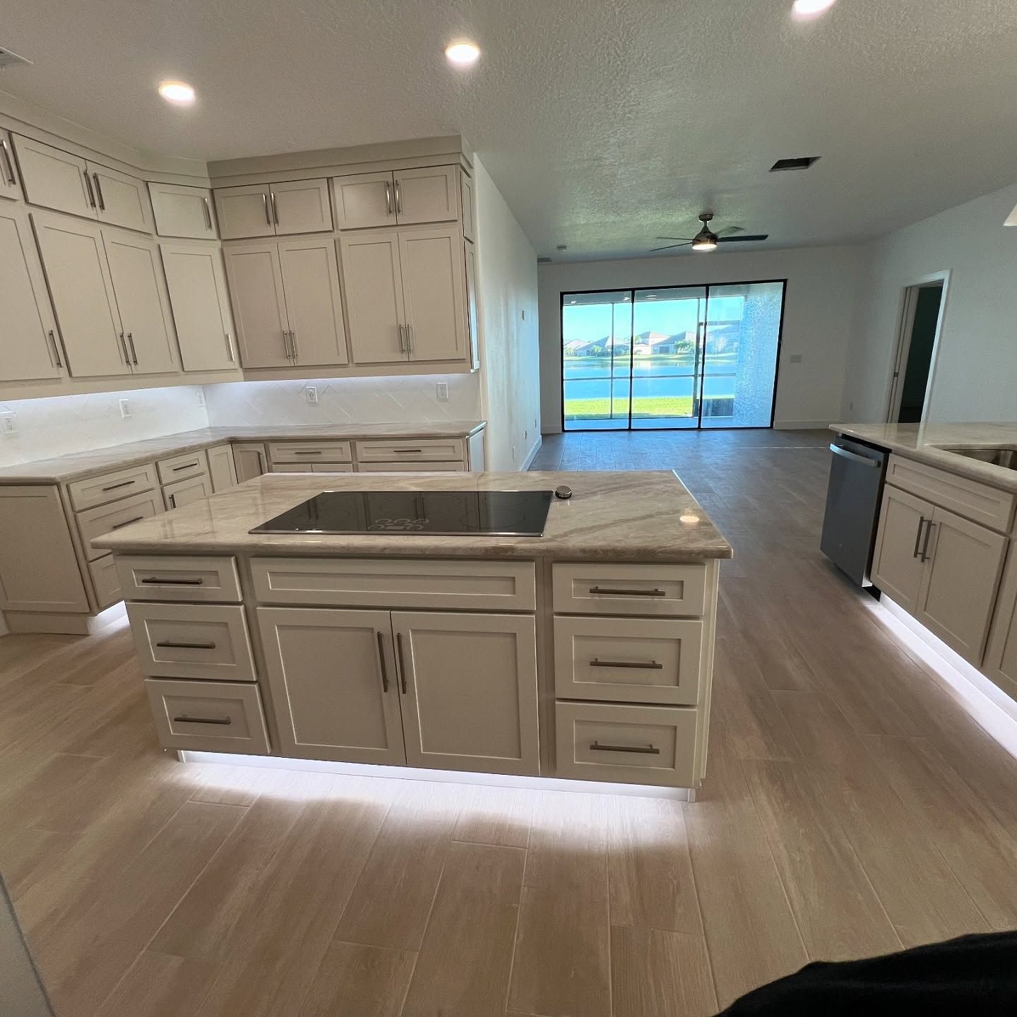 Modern kitchen with light wood floor, white cabinets, and large island with cooktop.