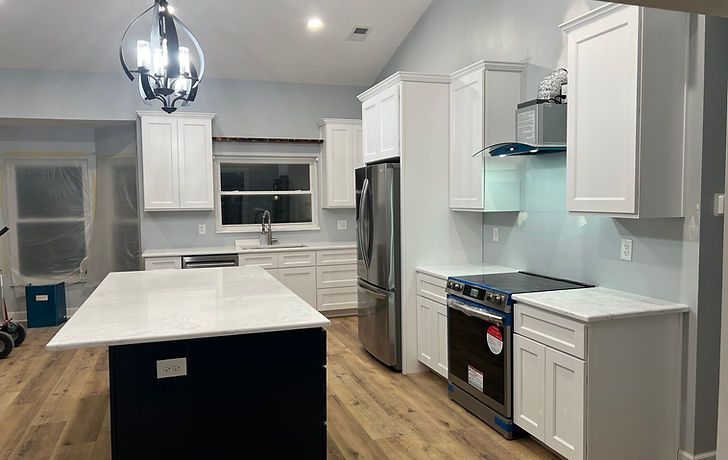 Modern kitchen with white cabinets, a large white island with a navy base, stainless appliances, and light wood floors.
