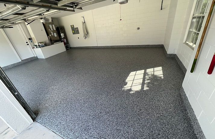 A garage interior with a glossy, grey, and white speckled epoxy floor coating and white painted block walls.