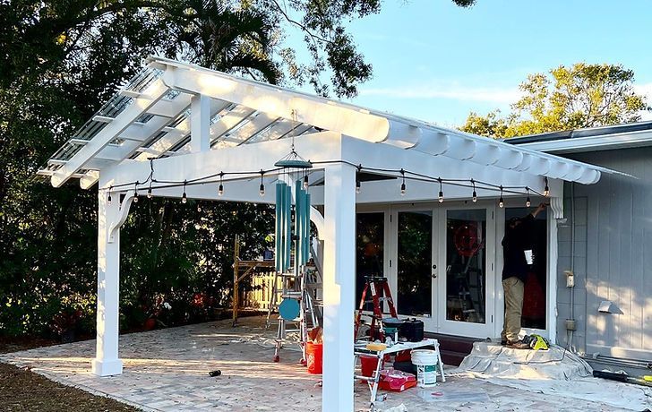 A newly constructed white pergola attached to a home, featuring a translucent roof and string lights over a patio.