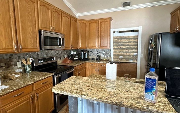 A kitchen with oak cabinets, granite countertops, stainless steel appliances, and a corrugated metal kitchen island base.