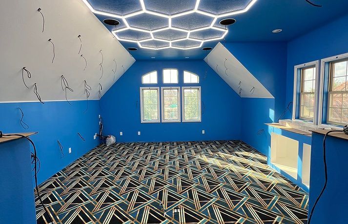 A room with blue walls, a geometric pattern carpet, and a futuristic honeycomb light fixture on the sloped ceiling.