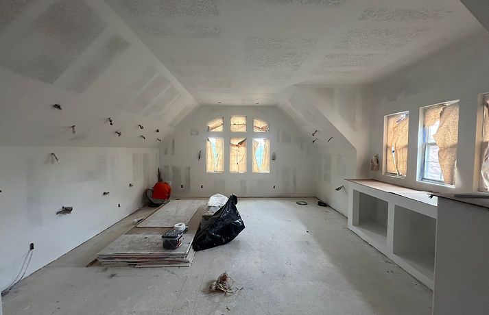 An attic room under construction with white drywall, a sloped ceiling, arched center window, and a built-in base unit.