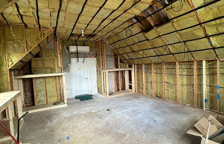 An unfinished attic room with exposed wooden framing, yellow insulation between studs, and a white door in the center.