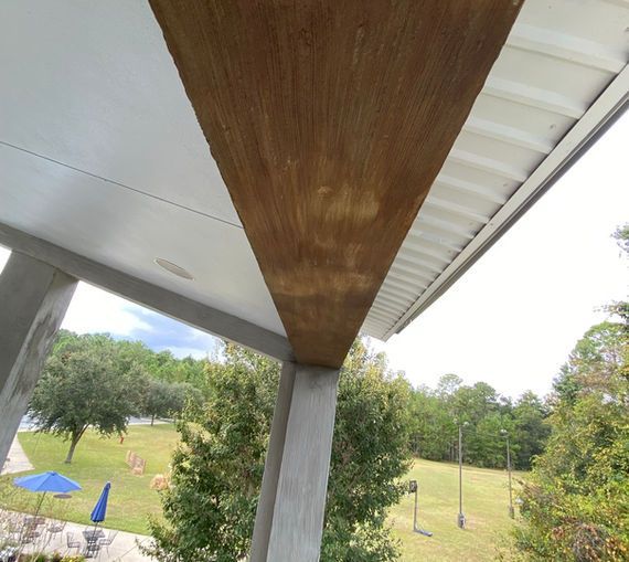 A wooden structural beam extends across the top of an outdoor covered porch overlooking a grassy landscape with trees.