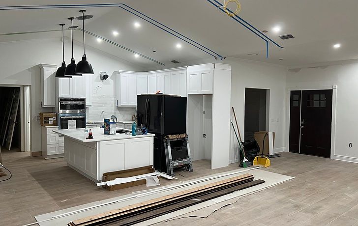 A kitchen under construction with white cabinets, a large island, stainless steel appliances, and wood-look tile flooring.