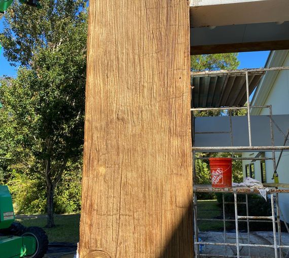 A large wooden post with a textured, stained finish stands outdoors next to scaffolding and a bucket.