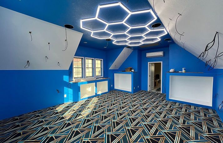 A room with blue walls, a geometric patterned carpet, and a large hexagon-shaped LED ceiling light fixture.