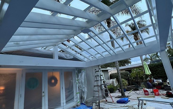 A newly painted white wooden pergola extends from a house, with plastic sheeting covering the doors and surrounding area.