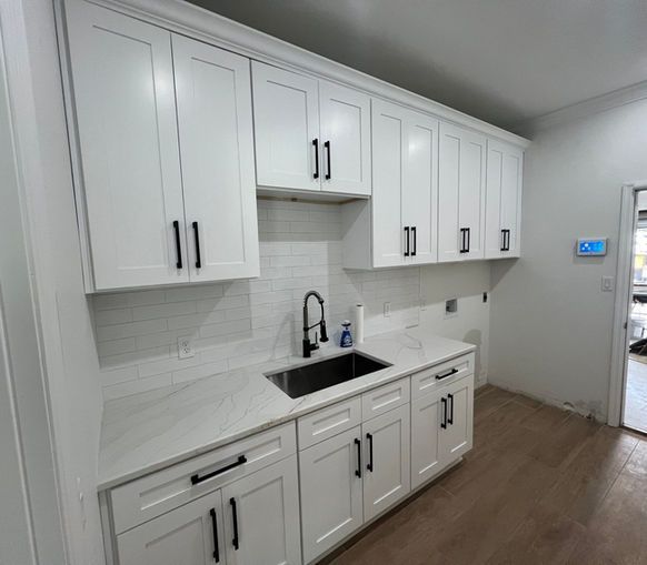 Modern kitchen featuring white shaker cabinets, matte black hardware, a stainless steel sink, and light countertops.