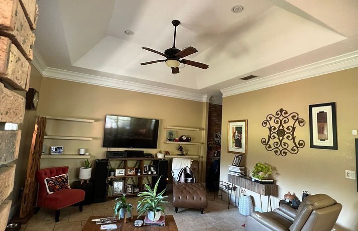 A living room with a tray ceiling, a television on a wooden media unit, seating, decorative shelves, and wall art.