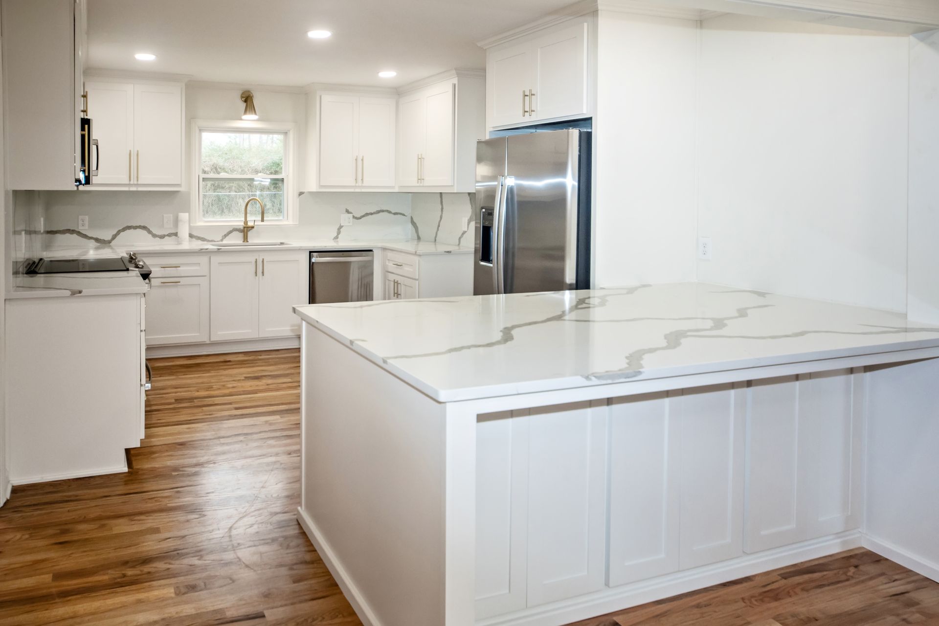 White kitchen with marble countertops, wood floor, stainless steel fridge, and island.