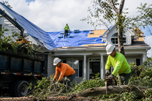 Roofing crew working on a house with a blue tarp and debris cleanup after storm damage