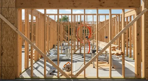 Framed house interior under construction with exposed wooden studs and a concrete floor.