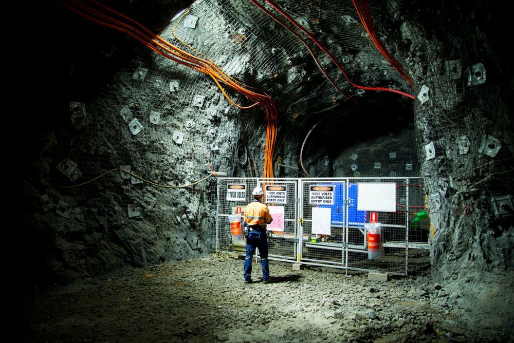 Worker in a Dim, Rocky Tunnel Stands Before Safety Signs and Wires — Tincone Pty Ltd in Paget, QLD