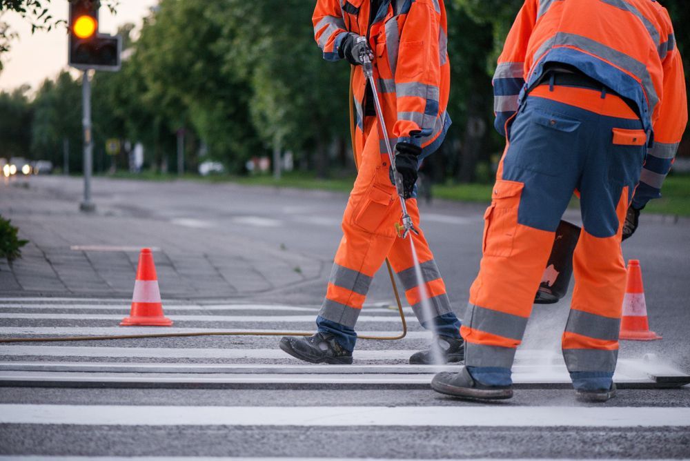 Road Workers in Orange Safety Suits Painting a Crosswalk With White Lines — Tincone Pty Ltd in Paget, QLD