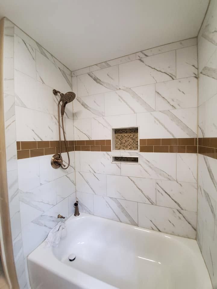 Small tiled bathroom with a white bathtub, bronze trim, and a handheld shower on the wall.