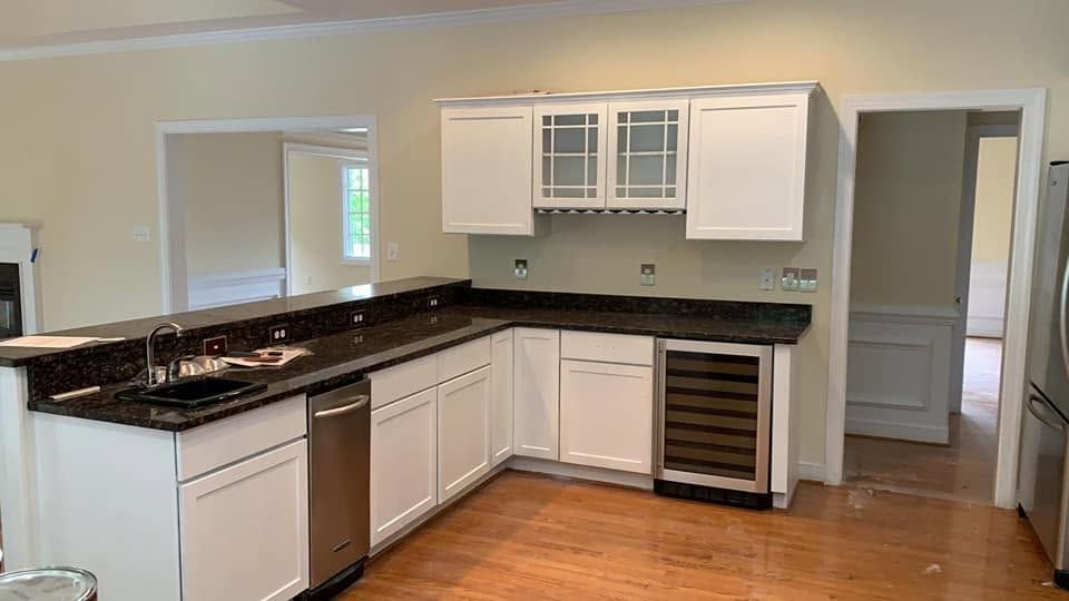 Empty modern kitchen with white cabinets, black countertops, and wood floors, viewed from the dining area