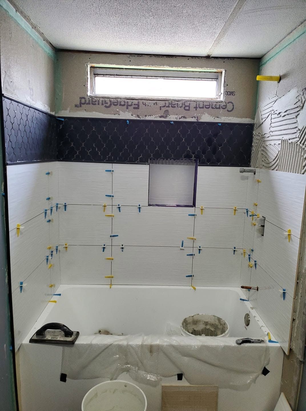 Tiled bathroom shower under renovation with exposed wall anchors and a small window above the shower head area
