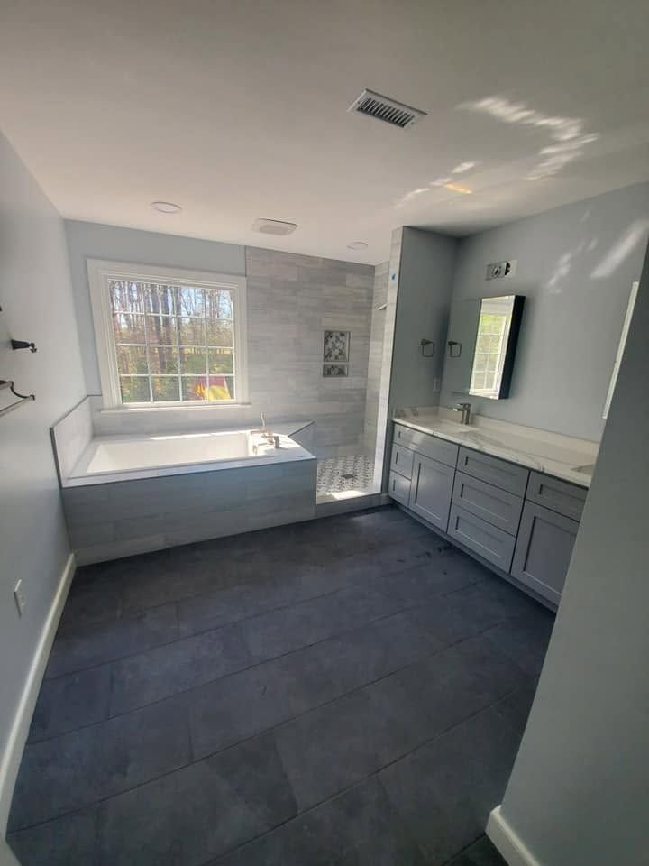 Bright bathroom with a window, built-in tub, vanity, and dark tile floor.