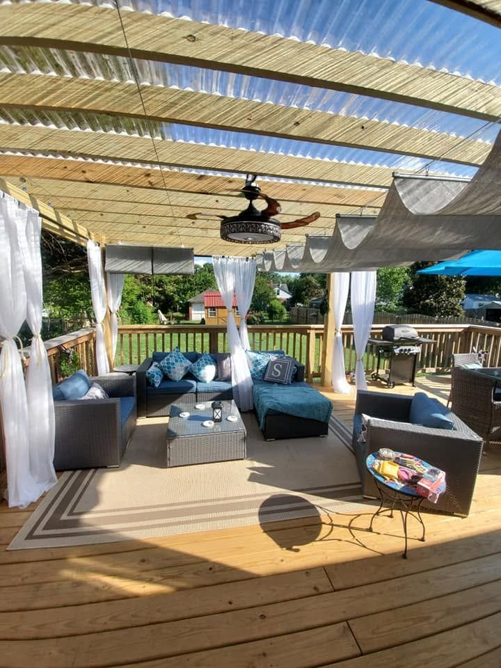 Outdoor patio with gray sectional seating, wooden deck, and pergola shade beside a pool or garden.